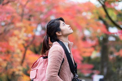 Woman looking away while standing against tree during autumn