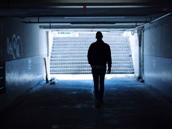 Rear view of man walking in illuminated corridor