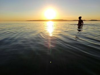 Silhouette person standing in sea against sky during sunset