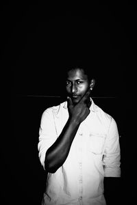 Portrait of young man standing against black background