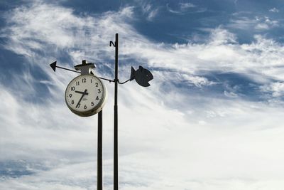 Low angle view of weather vane against cloudy sky