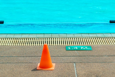 Orange cone and depth mark sign at a poolside of a local swimming pool