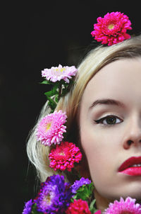 Close-up portrait of young woman with flowers on head against black background
