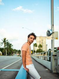 Portrait of young man leaning on railing against sky