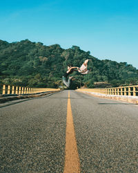 Woman jumping on road against clear sky