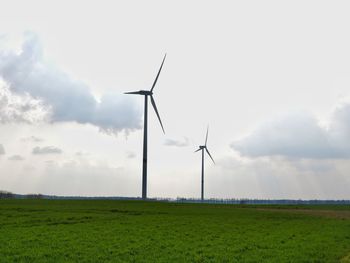 Low angle view of wind turbines on field against sky