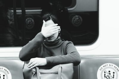 Young woman covering eyes while sitting at train