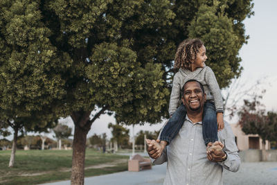 Joyful son sitting on a happy father's shoulders at park playground