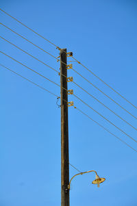 Low angle view of electricity pylon against blue sky