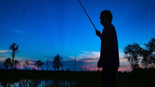 Silhouette man standing on field against blue sky