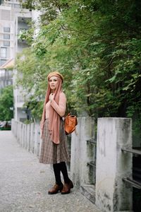 Woman looking away while standing on footpath against trees