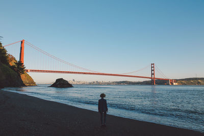 Woman standing on shore against golden gate bridge