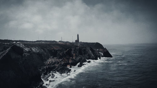 Lighthouse on rock formation in sea against sky