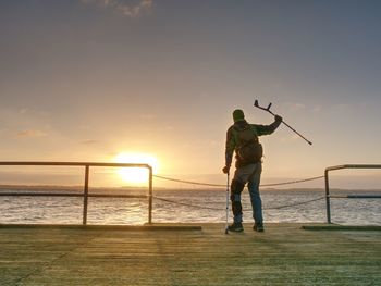 Traveler with backpack walk dificult with medicine poles. young tourist on bridge near sea at sunset