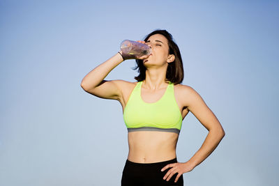 Woman drinking water while standing against clear sky