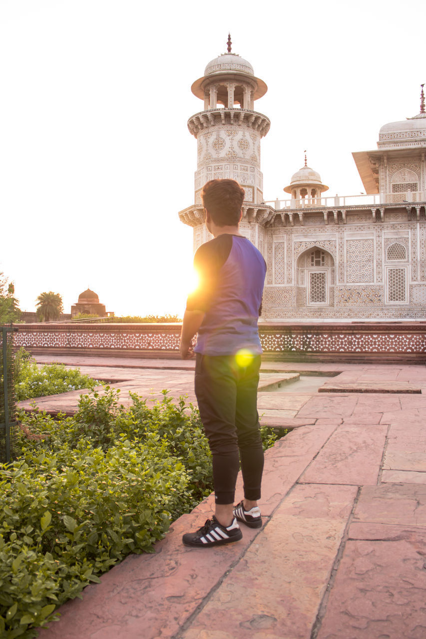 FULL LENGTH REAR VIEW OF MAN STANDING ON FOOTPATH AGAINST SKY