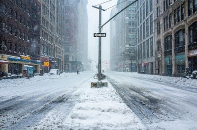 Street covered with snow amidst buildings in city during snowfall