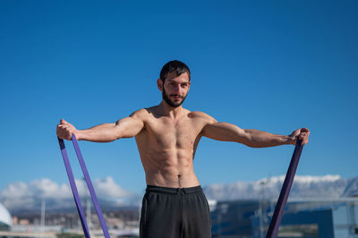 Shirtless man doing loop exercises outdoors. 