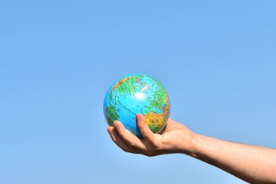 Cropped hand of man holding globe against clear blue sky