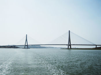 Suspension bridge over sea against clear sky