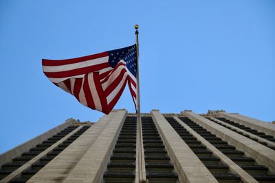 Low angle view of flag against buildings against clear blue sky