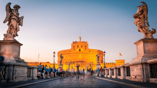 People on bridge leading towards historic building against sky