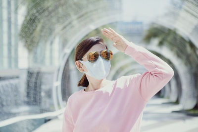Woman wearing mask and sunglasses shielding eyes outdoors