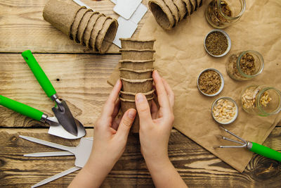 Women's hands hold peat pots. top view of seeds and garden tools on a wooden background.