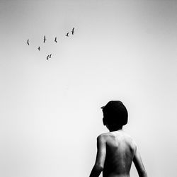 Rear view of shirtless boy standing against clear sky