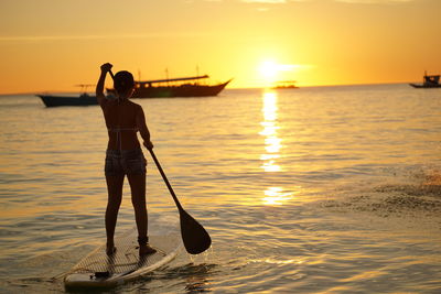 Rear view of silhouette person standing in sea against sky during sunset