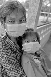 Portrait of grandmother and granddaughter wearing mask sitting at corridor