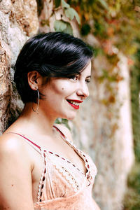 Smiling young woman standing by wall standing outdoors