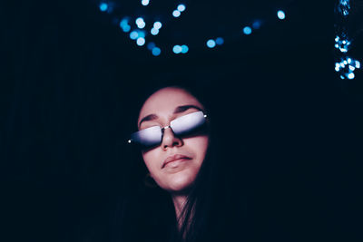 Confident young woman wearing sunglasses at illuminated restaurant