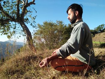 Side view of young man meditating while sitting on grass