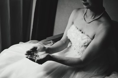 Midsection of bride wearing wedding dress holding ring while sitting on chair