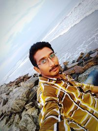 Portrait of young man standing on beach against sky