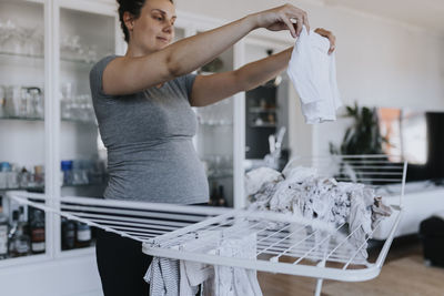 Pregnant woman doing housework and hanging baby clothes on drying rack