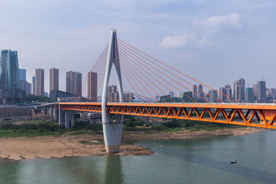 Suspension bridge over river and buildings against sky