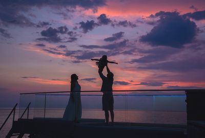 Silhouette people standing by sea against sky during sunset