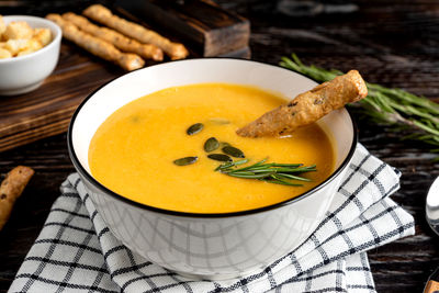 Pumpkin and carrot soup with cream, pumpkin seeds, croutons and grossini bread sticks on dark table