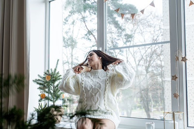Young woman standing by window at home