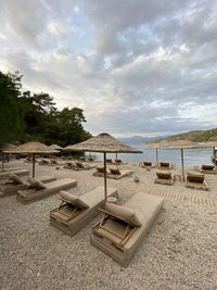 Lounge chairs by swimming pool at beach against sky