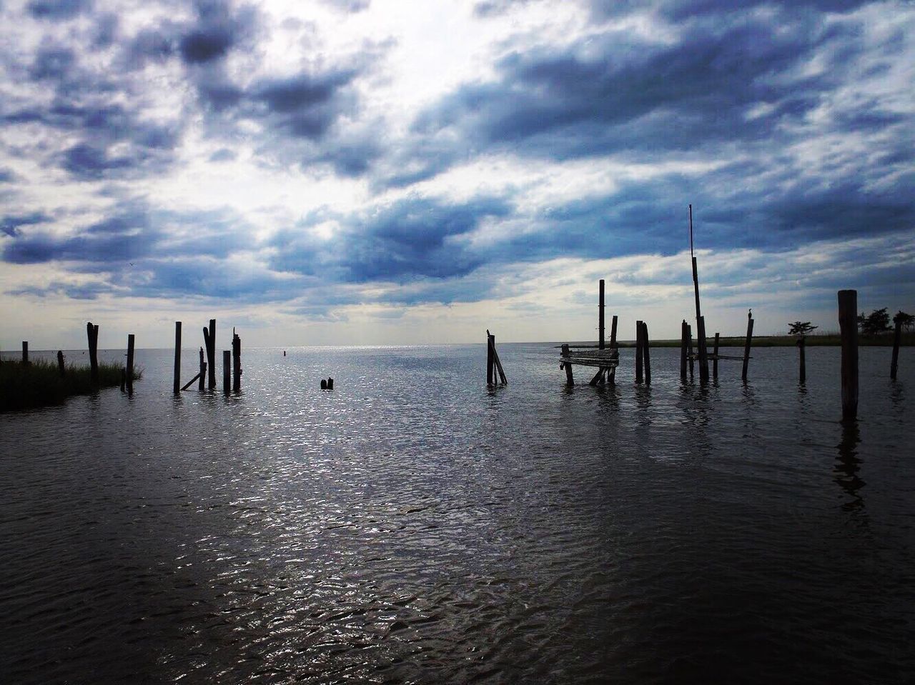 WOODEN POSTS ON SEA AGAINST SKY