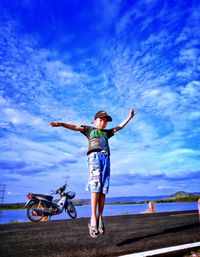 Full length of boy with arms outstretched jumping on road against sky