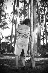 Rear view of woman standing by tree trunk in forest