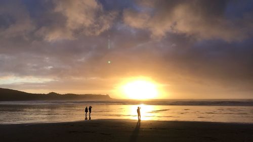 Silhouette people on beach against sky during sunset