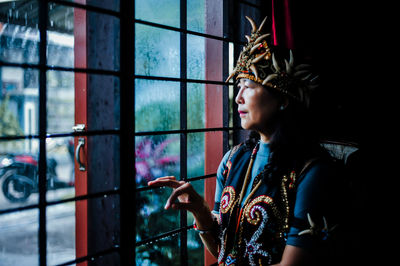 Portrait of young woman looking through window