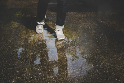 Low section of person standing on wet puddle during rainy season