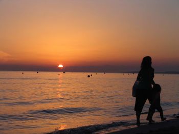 Silhouette people on beach against sky during sunset