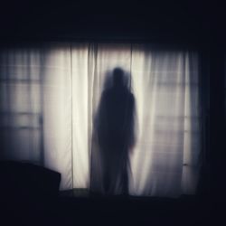 Silhouette woman standing by window in dark room